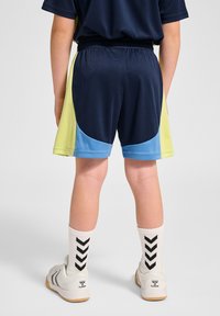 Marinablå shorts med gröna och blå sidopaneler, elastisk midja, parat med vita strumpor som har ett svart zigzag-mönster och lätta sneakers.