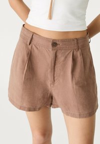 Pantaloni corti in lino marroni con una vestibilità rilassata, caratterizzati da un design plissettato e una chiusura con un solo bottone sul davanti. Orlo all'altezza del mezzo coscio.