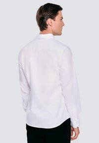 Biała koszula z długim rękawem w prostym fasonie, z wykładanym kołnierzykiem i mankietami zapinanymi na guziki, wykonana z lekkiego materiału. Gładka faktura.