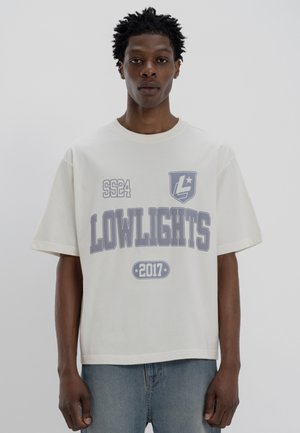Light beige oversized t-shirt made of cotton features bold gray text and logo designs, with a ribbed crew neckline and short sleeves.