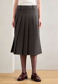 Jupe grise plissée, de longueur genou, en tissu texturé. Dotée d'une taille ajustée et d'une fente latérale subtile. Assortie à des chaussures bordeaux brillantes.
