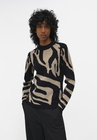 Gebreide trui met een zwart en beige zebra strepenpatroon, ronde halslijn en lange mouwen. Lichtgewicht stof met een zachte textuur.