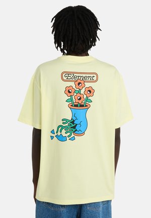 T-shirt jaune surdimensionné avec un motif représentant un vase bleu aux bords fissurés et des fleurs, avec le texte « Element » au-dessus. Matière en coton.