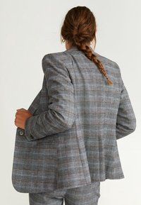 Blazer à carreaux gris en tissu texturé, doté d'une fermeture à boutons, d'épaules structurées et d'une coupe décontractée avec une fente arrière.