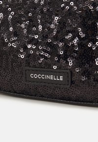 Svart paljetterad clutchväska med en slät läderetikett som visar varumärkesnamnet "COCCINELLE" i vit skrift.