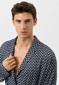 Chemise bleu marine à motif avec col châle, présentant de petits designs bleu clair. Fabriquée dans un tissu lisse, avec une coupe décontractée et un devant ouvert.