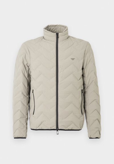 Ανοιχτό γκρι μπουφάν με σχέδιο καπιτονέ, υψηλό γιακά, εμπρόσθιο φερμουάρ, δύο πλαϊνές τσέπες και μαύρες λεπτομέρειες γύρω από το φερμουάρ και το τελείωμα.