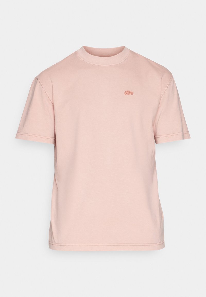 T-shirt à col rond à manches courtes, couleur rose pâle, avec un petit logo de crocodile brodé sur la poitrine gauche.