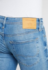 Ljust blå denimjeans med skräddarsydd passform. Har en läderpatch med märket "JACK&JONES" och synlig sömnad på bakfickorna.