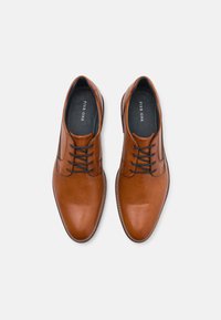 Braune Lederhausschuhe mit glatter Oberfläche, runder Zehenpartie und kontrastierenden schwarzen Schnürsenkeln. Verfügt über eine genähte Sohle und einen leichten Absatz.