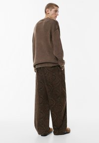 Brun oversized tröja med texturerad tyg, kombinerad med mönstrade vida byxor som har en blommig design i mörkare nyanser.