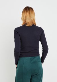 Marineblå langermet tettsittende topp med rund hals, kombinert med grønne høytlivsbukser. Glatt tekstur og enkelt design uten mønstre.