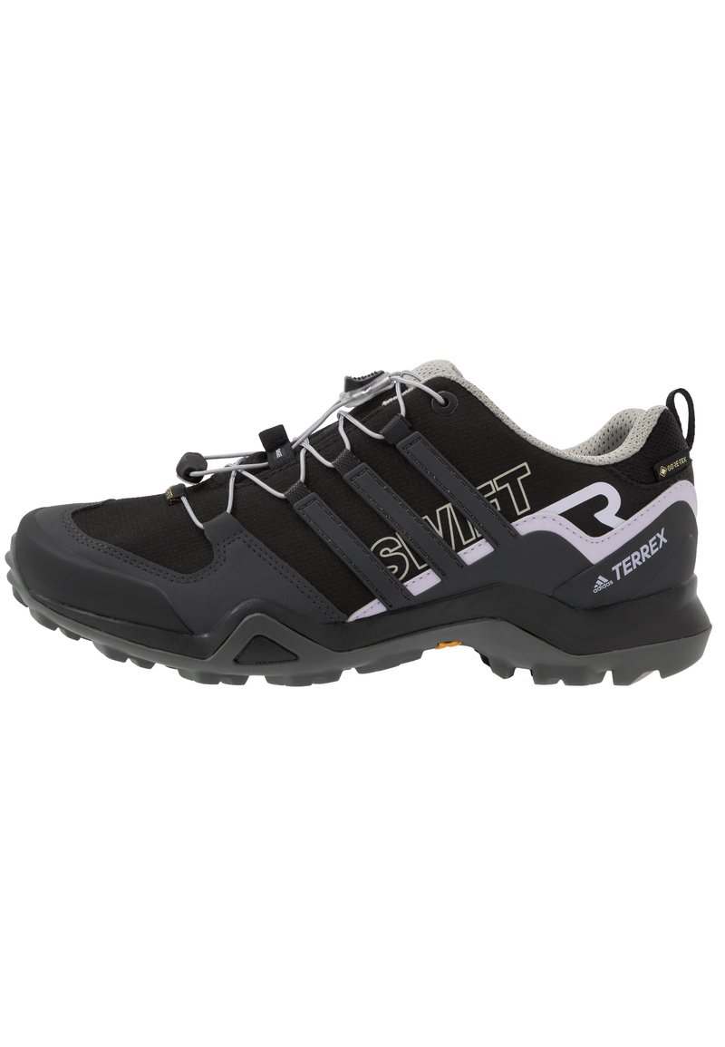Zapato exterior negro con acentos grises, parte superior de malla y suela de goma. Presenta cordones elásticos, tres rayas en el costado y un talón acolchado.