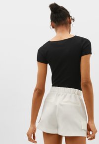 Black ribbed short-sleeve top paired with white elastic-waist shorts featuring rear pockets and a smooth texture. Back view shown.