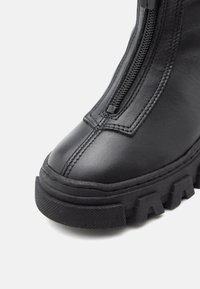 Bottine en cuir noir avec une semelle épaisse, fermeture éclair et accents texturés contrastés sur la plateforme et le dessus.