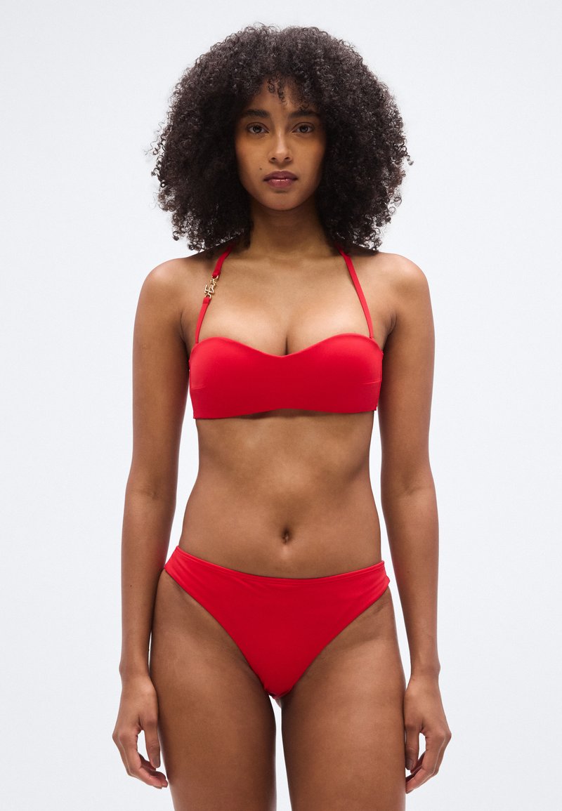 Κόκκινο μπικίνι δύο τεμαχίων από λείο ύφασμα. Το πάνω μέρος διαθέ τει δομημένο σχέδιο bandeau, ενώ το κάτω μέρος είναι κλασικό και χαμηλοκάβαλο.