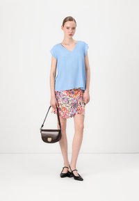 Top blu corto a maniche corte, gonna mini a fiori dai colori vivaci, scarpe nere con cinturini, e una borsa a tracolla marrone scuro con un accento metallico.