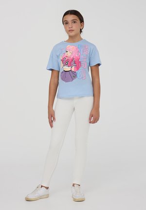T-shirt azzurro a maniche corte con un vivace design grafico di una ragazza con capelli rosa e occhiali da sole, abbinato a leggings bianchi e sneakers.