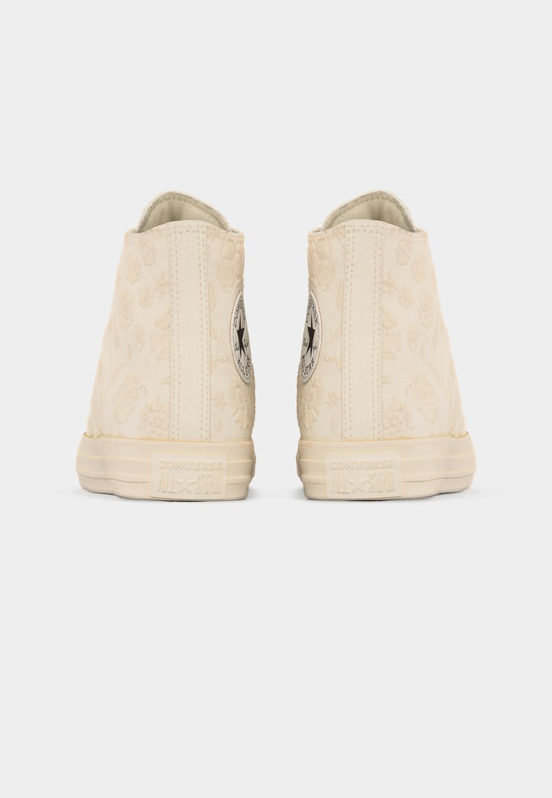 Paar beige hohe Converse-Sneaker, von hinten betrachtet, mit dezenten Blumenmustern und markenspezifischen Gummisohlen.