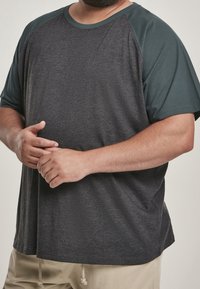 Ciemnoszary T-shirt z krótkimi rękawami, raglanowy projekt w ciemnej zieleni. Miękka tekstura tkaniny, luźny krój, brak widocznych wzorów lub logo.