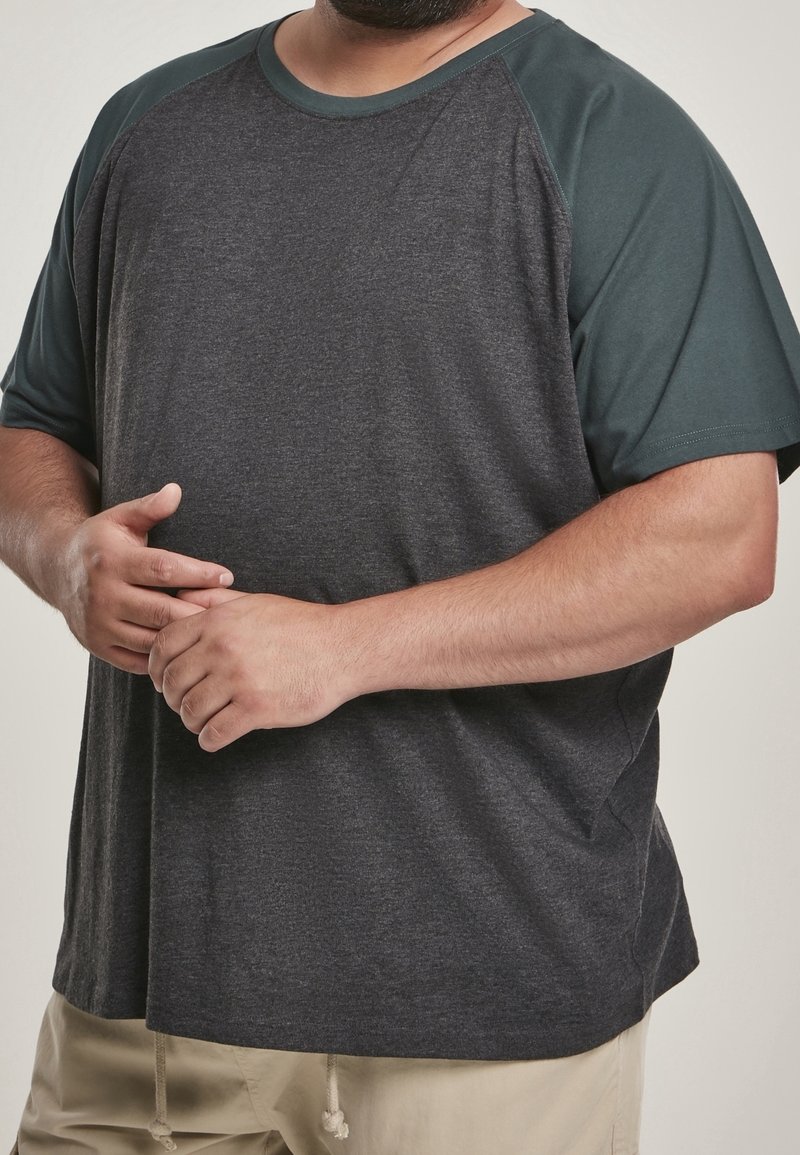 Ciemnoszary T-shirt z krótkimi rękawami, raglanowy projekt w ciemnej zieleni. Miękka tekstura tkaniny, luźny krój, brak widocznych wzorów lub logo.