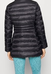 Svart puffjacka med figurnära design, horisontell quiltad textur och hög krage. Bärs över aqua orm-mönstrade leggings.