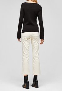 Svart ribbad tröja, krämfärgade vida byxor i mjukt tyg, svarta ankelskor med texturerad yta och klackar.