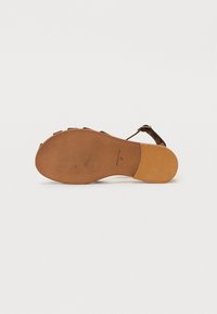 Sandale en cuir marron avec une semelle plate, présentant un design texturé et une bride cheville. La semelle a une base en caoutchouc pour l'adhérence.
