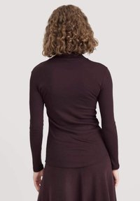 Langdurige, aansluitende coltrui met lange mouwen in donkerpaars. Zachte, gladde stof met een subtiele glans. Heeft een hoge kraag en smal aansluitende mouwen.