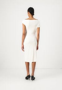 White midi dress with an off-the-shoulder neckline, fitted design, and short sleeves. Worn with black high-heeled shoes. Smooth texture.