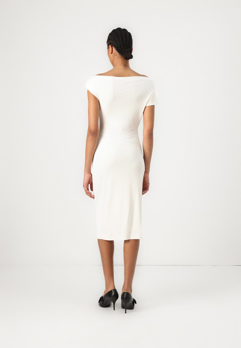 Robe midi blanche avec un décolleté épaules nues, design ajusté et manches courtes. Portée avec des chaussures à talons hauts noires. Texture lisse.