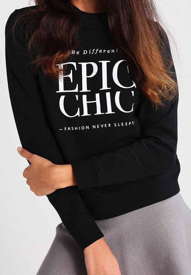 Femme portant un sweat-shirt noir avec le texte "Be Different EPIC CHIC - Fashion Never Sleeps" et une jupe grise.