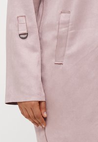 Light pink, smooth fabric jacket featuring a cuff with a ring detail, and a side pocket. The texture appears soft and slightly shiny.