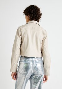 Beige faux lærher cropped jakke med krage, lange ærmer og subtile syninger, kombinert med metallisk sølvfargede høytaljede jeans.