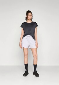 T-shirt cinzento escuro de mangas curtas combinado com calções roxos claros com cordão. Meias pretas e sapatos pretos completam o conjunto.