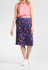 Rosa ärmlös blus med spetsdetaljer; plisserad marinblå kjol med röd blommönster; vita sneakers fulländar outfiten.