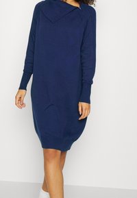 Abito lavorato a maglia blu navy con colletto ripiegato, maniche lunghe e dettagli a coste lungo i fianchi e i polsini. Presenta una vestibilità rilassata.