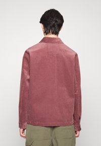 Korte jas van ribstof in stofroze met verticale strepen, een puntige kraag en knoopsluitingen bij de manchet. Heeft een relaxte fit en een textiele stof.