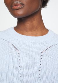 Maglione azzurro chiaro in maglia con un motivo testurizzato, scollatura rotonda e dettagli a forma di taglio sulle spalle. Tessuto morbido e leggero.