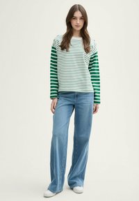 Camisa de manga larga a rayas en colores verde y blanco, combinada con jeans de pierna ancha de un azul claro y zapatillas blancas. Diseño de atuendo casual.