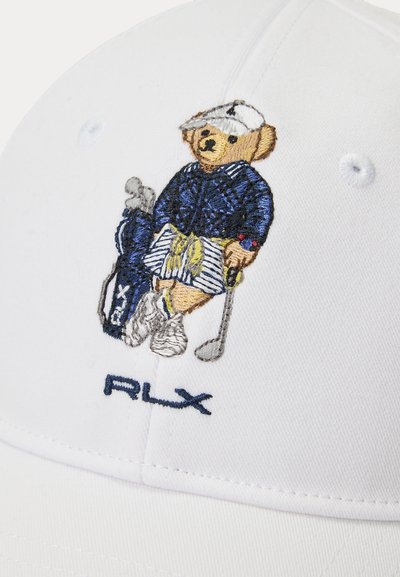 Κεντητή αρκούδα με γκολφ ενδυμασία και καπέλο, κρατώντας ένα γκολφ μπαστούνι δίπλα σε μια τσάντα γκολφ, πάνω σε ένα λευκό καπέλο με το κείμενο "RLX" από κάτω.