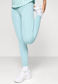 Lys blå Nike tights med en glatt tekstur, med en diskret logo, kombinert med hvite treningssko og hvite sokker.