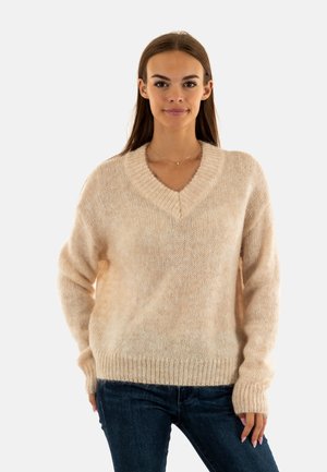 Maglione lavorato a maglia beige chiaro con scollatura a V e maniche lunghe. Texture morbida e polsini a coste. Abbinato a jeans blu scuro.