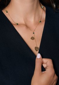 Złoty naszyjnik z dwoma zawieszkami w kształcie liści i zielonymi kamieniami szlachetnymi. Delikatny design łańcuszka, z naprzemiennymi elementami dekoracyjnymi.