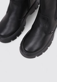 Bottes noires en cuir au niveau de la cheville avec une semelle en caoutchouc texturée et robuste, présentant un bout rond et des coutures discrètes.