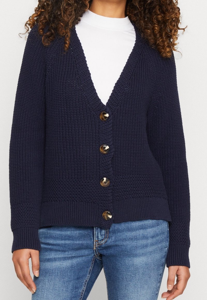 Cardigan lavorato a maglia blu navy con scollo a V, sette bottoni dorati sul davanti e polsini e orlo a coste. Tessuto con motivo testurizzato in tutto il capo.