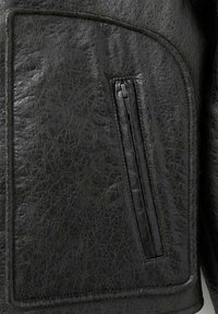 Chaqueta de cuero negra con una superficie texturizada, costuras curvas y un bolsillo con cremallera en el lado izquierdo. Acabado suave con un brillo sutil.