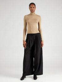 Beige Rollkragenpullover mit langen Ärmeln, kombiniert mit lockeren, hochtaillierten schwarzen Hosen, die eine glatte Textur und klare Linien aufweisen.