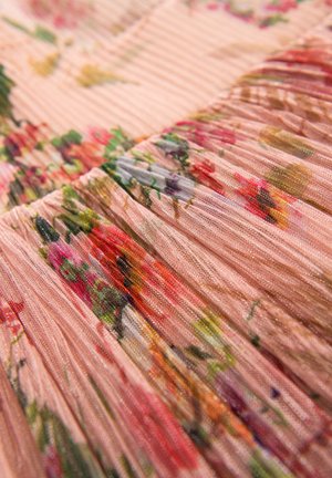 Organza kudosissa pehmeässä vaaleanpunaisessa, jossa on kukkakuvioita punaisen, vihreän ja keltaisen sävyissä. Materiaalin rakenne näyttää kevyeltä ja ilmavalta.