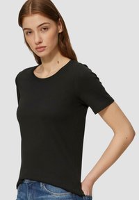 T-shirt nero a maniche corte in cotone morbido. Presenta un classico collo tondo e una silhouette aderente, indossato con jeans in denim blu.